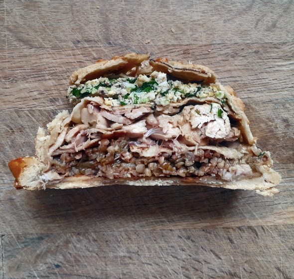 Cross-section slice of kurnik showing the traditional fillings of egg, chicken and buckwheat separated by pancakes.